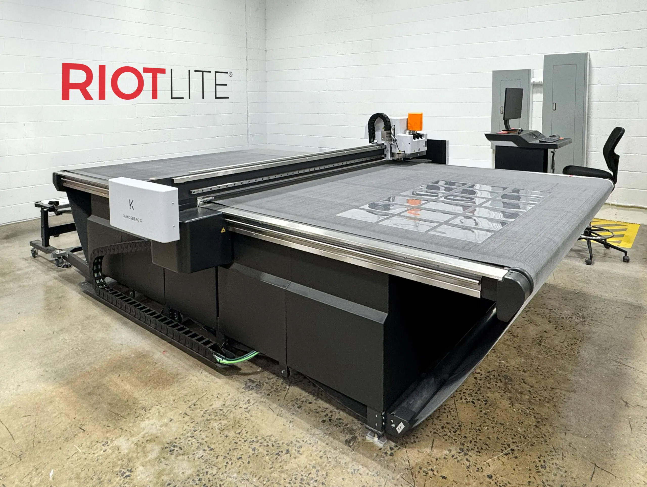 The RIOTLITE wall decal above the Kongsberg X flatbed cutter, with sheets of film nested on the bed.