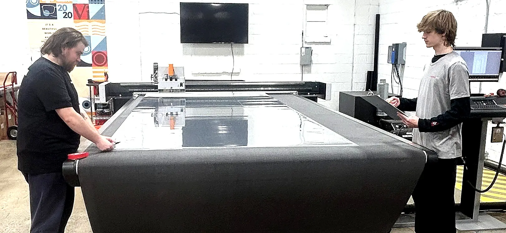 Two staff at the cutter table squaring a large clear film sheet.